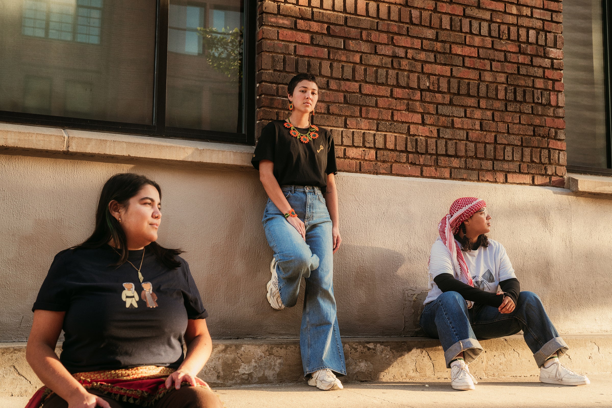 Three people posing on a ledge against a brick wall.
